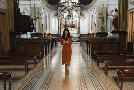 A woman walks down the aisle of an ornate church interior with chandeliers and benches.